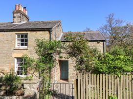 A stone cottage with a blue door surrounded by greenery and a metal gate at Whinstone Cottage Esk Valley near Grosmont