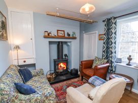 A small living room with a wood burning stove a patterned sofa two armchairs and a window with curtains at Whinstone Cottage Esk Valley near Grosmont