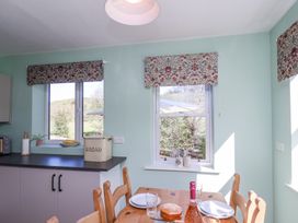 A kitchen with floral window blinds a wooden dining table set with plate a cake and a bottle at Whinstone Cottage Esk Valley near Grosmont