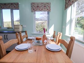 A dining area with a wooden table set with plates glasses a bottle of prosecco and a cake near windows with floral blinds at Whinstone Cottage Esk Valley near Grosmont