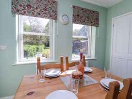A dining room with a wooden table set with plates glasses and a cake near two windows with floral blinds at Whinstone Cottage Esk Valley near Grosmont