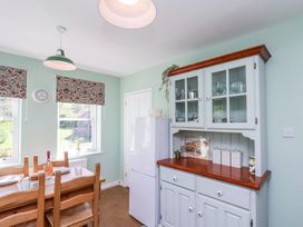 A kitchen with a wooden dining table set by two windows and a white cabinet with glass doors at Whinstone Cottage Esk Valley near Grosmont