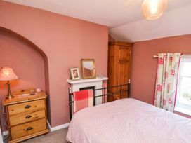 A bedroom with a bed a wooden dresser a lamp a cupboard and floral curtains at Whinstone Cottage Esk Valley near Grosmont