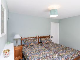 A bedroom with two single beds with patterned bedding a wooden nightstand with a lamp and a white door at Whinstone Cottage in Esk Valley near Grosmont