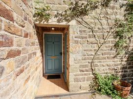 A blue door with the number 2 set in a stone wall with a tiled floor and a wooden planter nearby at Whinstone Cottage in Esk Valley near Grosmont