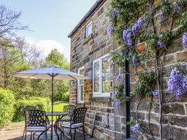 An outdoor patio with a table four chairs and a large umbrella next to a stone wall with climbing purple flowers at Whinstone Cottage in Esk Valley near Grosmont