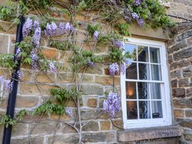 A stone wall with a white window framed by purple flowering vines at Whinstone Cottage in Esk Valley near Grosmont