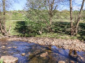 A flowing stream with rocks along the bank and trees on grassy land at Whinstone Cottage Esk Valley near Grosmont