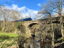 A train crossing a bridge over a river in a forested area near Esk Valley near Grosmont
