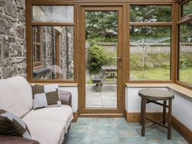 A conservatory with a sofa and table overlooking a garden at Cove Cottage Llangrannog