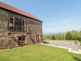 Stone cottage with wooden window frames and flower pots on a grassy lawn with trees and countryside in the background at Newlands Barn in Wellington