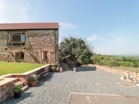 The exterior of a stone building with windows and a gravel driveway with flower pots and a bench at Newlands Barn in Wellington