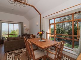 A dining table with chairs and a vase of flowers next to large windows and a seating area with sofas in a room at Newlands Barn in Wellington