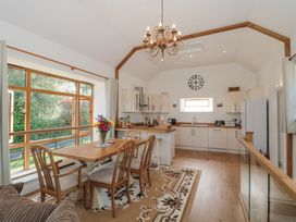 A kitchen and dining area with wooden table, chairs, chandelier, large window, and kitchen cabinets at Newlands Barn in Wellington