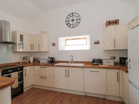 A kitchen with white cabinets wooden countertops a black stove a sink under a small window and various appliances at Newlands Barn in Wellington