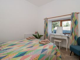 A bedroom with two beds covered in colorful patchwork quilts a white dressing table with a mirror and stool near a window with patterned curtains and a blue chair at Newlands Barn in Wellington
