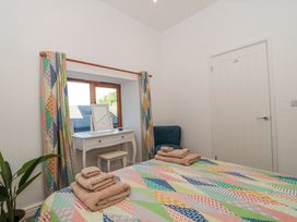 A bedroom with a bed covered by a patterned quilt and folded towels a white dressing table under a window with patterned curtains a green chair and a potted plant at Newlands Barn in Wellington
