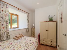 A bedroom with a bed covered with floral bedding a wardrobe and chest of drawers next to a window with floral curtains at Newlands Barn in Wellington