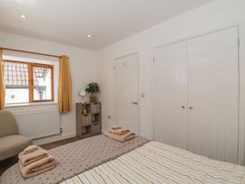 A bedroom with a bed, folded towels on the bed, a window with yellow curtains, a small cabinet with a plant and mirror, and white doors at Newlands Barn in Wellington