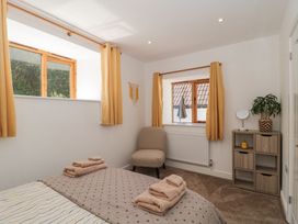 A bedroom with two windows yellow curtains a beige chair a small shelving unit with a plant and mirror and a bed with folded towels at Newlands Barn in Wellington