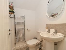 A bathroom with a toilet, pedestal sink, round mirror, towel radiator, and small wall shelf at Newlands Barn in Wellington
