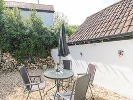 An outdoor patio with four chairs around a glass table with a bottle and glasses and a closed umbrella at Newlands Barn in Wellington