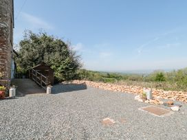 An outdoor gravel area with a wooden shed and stone wall overlooking a green landscape at Newlands Barn in Wellington