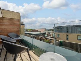 A balcony with three black chairs and a round table overlooking buildings and the sea at Ebbtide in Newquay