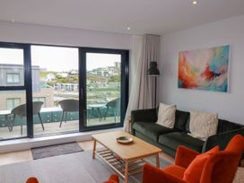 A living room with a green sofa, orange armchair, wooden coffee table, and balcony with chairs at Ebbtide in Newquay