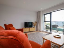 A living room with red armchairs a wooden coffee table a television on a stand and sliding glass doors leading to a balcony at Ebbtide in Newquay