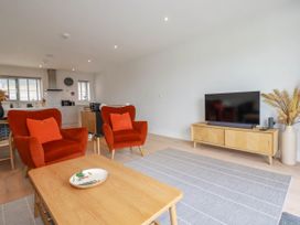A living room with two orange armchairs a wooden coffee table and a TV unit at Ebbtide in Newquay