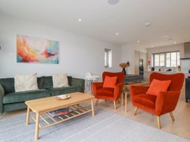A living room with a green sofa and two orange armchairs a wooden coffee table and a kitchen in the background at Ebbtide in Newquay