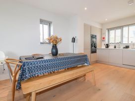 A dining area with a table covered by a blue patterned tablecloth surrounded by chairs and a bench next to a kitchen with built in appliances at Ebbtide in Newquay