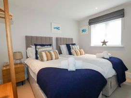 A bedroom with two single beds with pillows and towels a window with a blind and a wooden side table with a lamp at Ebbtide in Newquay