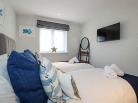 A bedroom with two single beds pillows and blankets a wall mounted tv and a window with a black blind at Ebbtide in Newquay