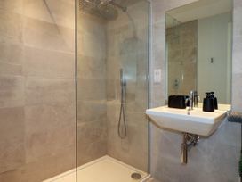 A bathroom with a walk in shower and a wall mounted sink with black accessories at Ebbtide in Newquay