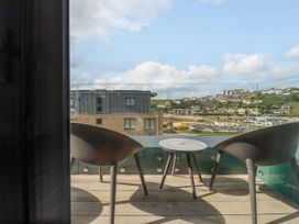 A balcony with two chairs and a small round table overlooking buildings and a hillside at Ebbtide in Newquay