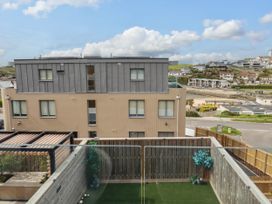 A balcony with artificial grass and plants overlooking a modern building and a coastal town at Ebbtide in Newquay