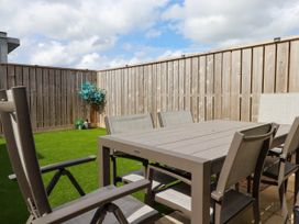 An outdoor patio area with a dining table and chairs on artificial grass with wooden fencing at Ebbtide in Newquay