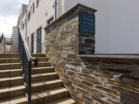 An exterior stone wall with a sign that reads ebb tide next to stairs and a building in Newquay