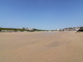 A wide sandy beach with houses and greenery in the background at Ebbtide in Newquay