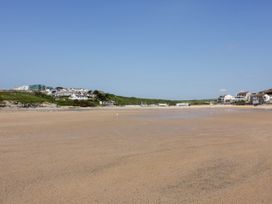 A wide sandy beach with buildings and green hills in the background at Ebbtide in Newquay