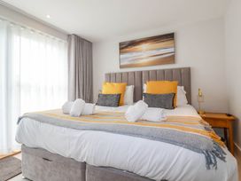 A bedroom with a large bed yellow and gray pillows and a sunset painting above at Ebbtide in Newquay