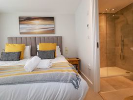 A bedroom with a bed with yellow and gray pillows next to a bathroom with a glass shower at Ebbtide in Newquay