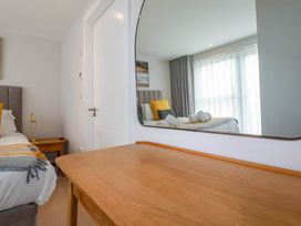 A bedroom with a wooden table and a large mirror reflecting a bed with pillows and rolled towels at Ebbtide in Newquay