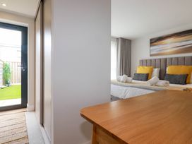 A bedroom with a bed with pillows and rolled towels a wooden table a door leading outside and a closed wardrobe at Ebbtide in Newquay