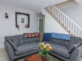 A living room with a grey sofa, throws and cushions, a wooden coffee table with flowers, stairs and a recessed wall shelf at Joymead in Malborough