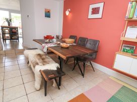 A dining area with a wooden table and chairs next to a coral colored wall with a framed picture and a wooden shelving unit at Joymead in Malborough