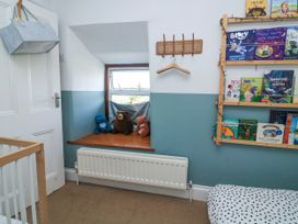 A children's room with a window seat holding stuffed animals a wall-mounted book shelf with children's books a white door with a gray hanging basket and a radiator below the window at Joymead in Malborough