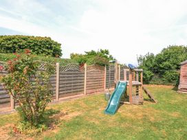 A backyard with a children's playset including a slide and climbing frame with a wooden fence and a bush at Joymead in Malborough